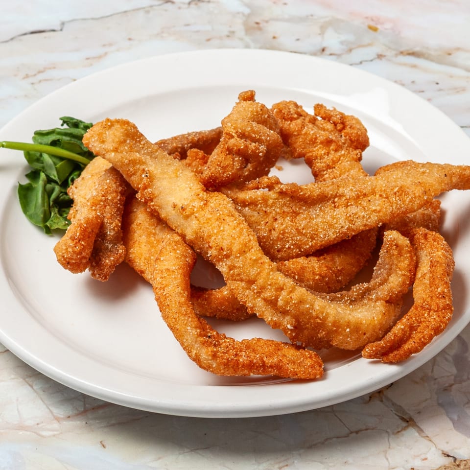 Crispy fried catfish fillets with a side of fresh spinach on a white plate.