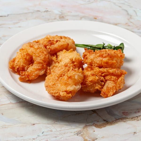 Golden-brown fried shrimp with a side of green garnish on a white plate.