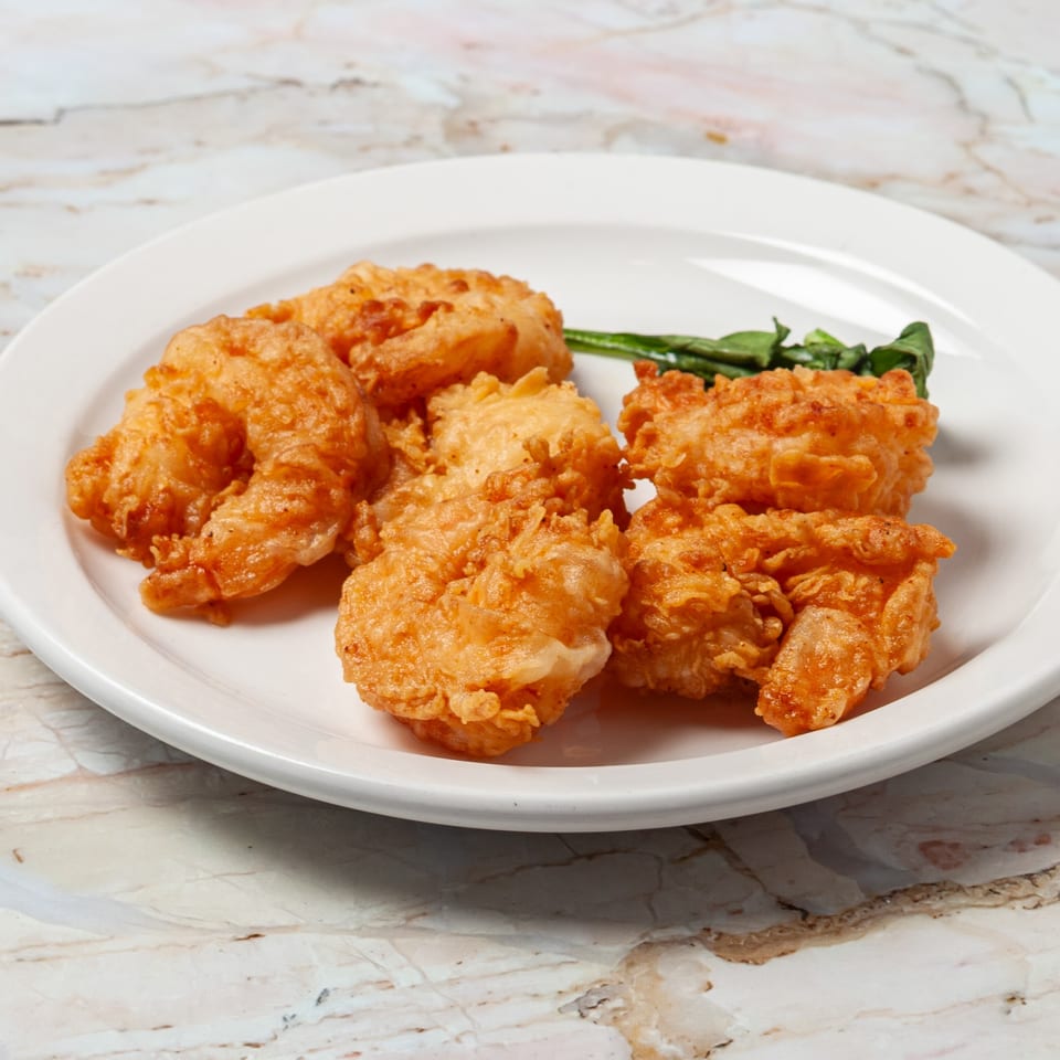 Golden-brown fried shrimp with a side of green garnish on a white plate.