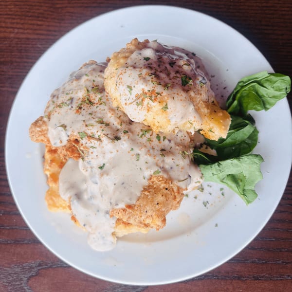 Golden-fried chicken and biscuits smothered in creamy gravy, garnished with herbs and a side of greens.