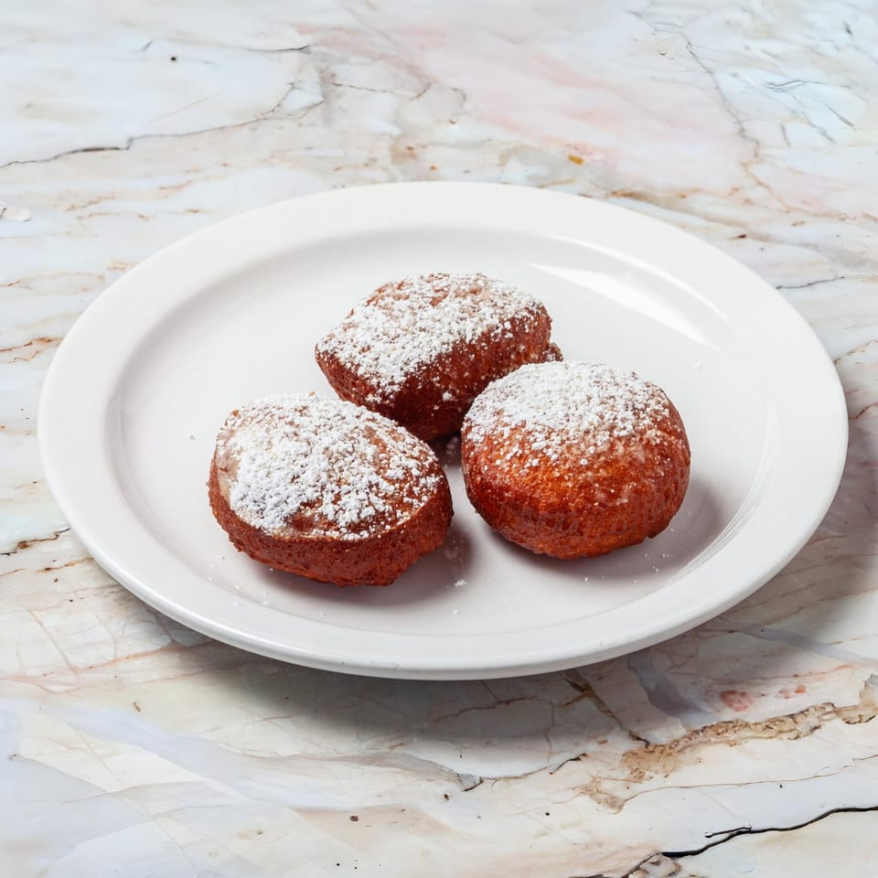 Three golden-brown beignets, dusted with powdered sugar, on a white plate.