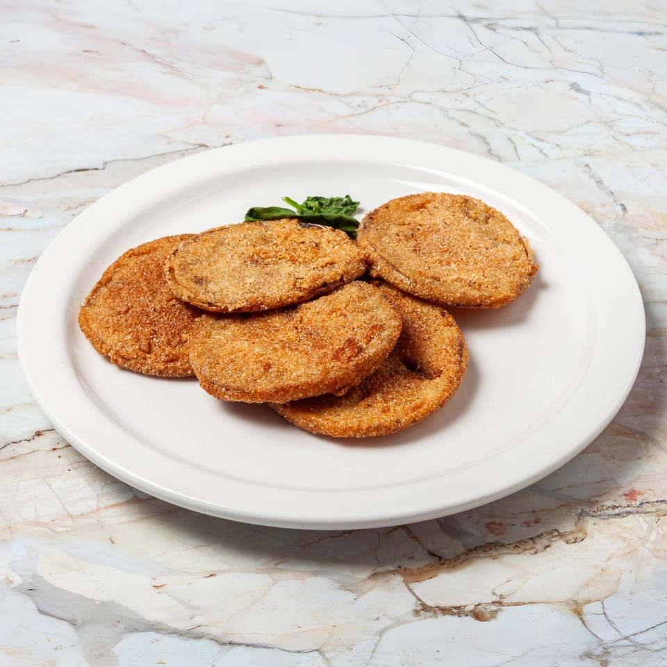 A white plate holds several golden-brown fried green tomatoes, garnished with a sprig of green herbs.