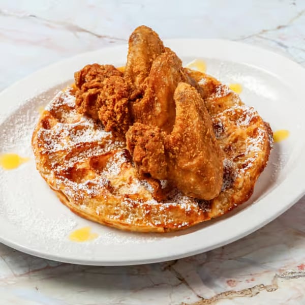 Golden-brown chicken and waffle, dusted with powdered sugar and drizzled with syrup on a white plate.